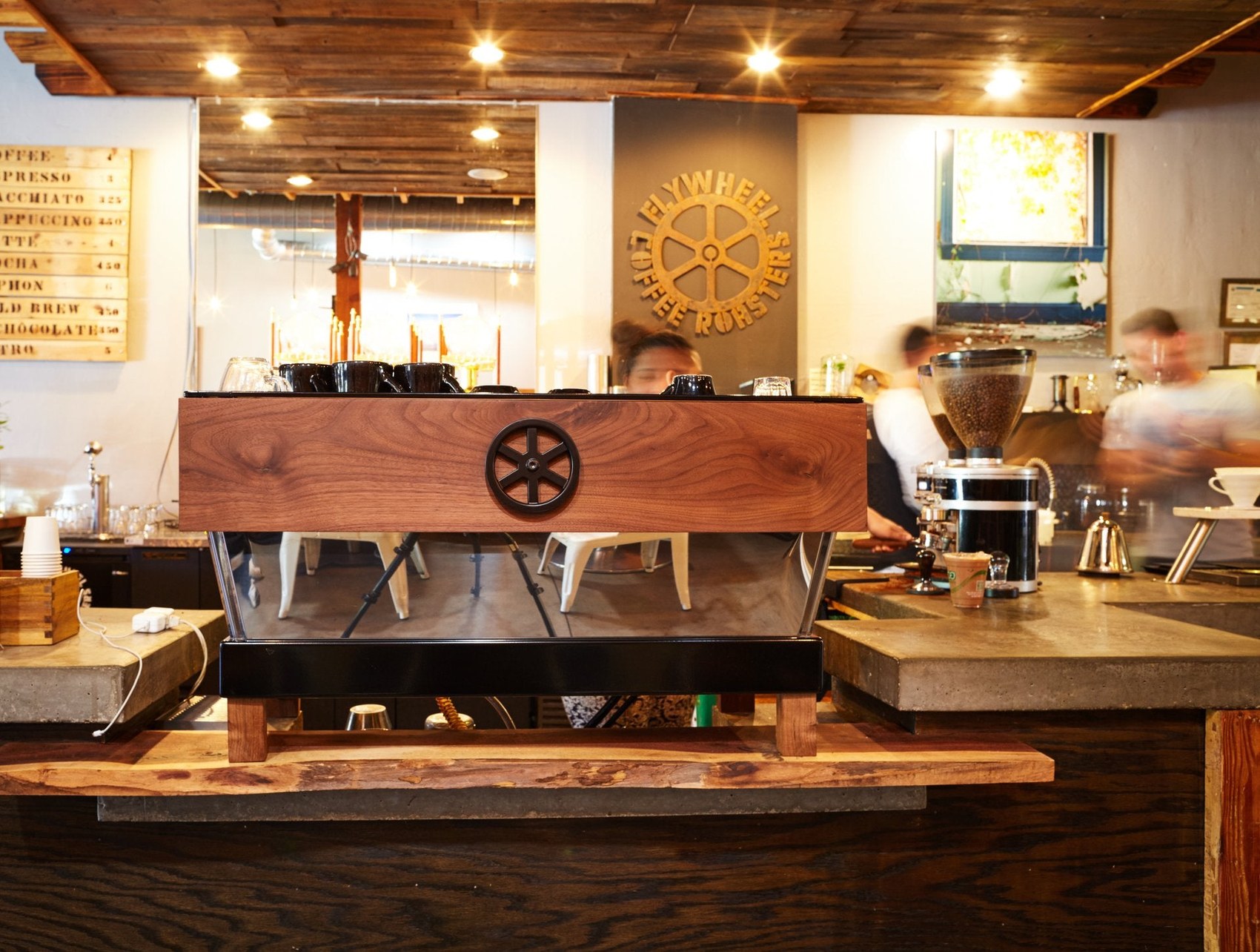The custom wood clad espresso machine at Flywheel Coffee Roasters, with the gear logo on the wall behind
